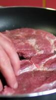 Step by step, a man cuts meat into steaks and fries them in a frying pan raw rib eye steaks with spices and herbs on a wooden kitchen table, sprinkle with sea salt and peppers on top. video