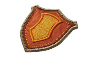 Close-up of an embroidered badge with orange and gold threads on a shield-shaped fabric. Ideal for fashion, military, and DIY projects. png