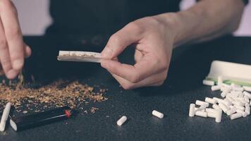 Man in Black Clothing is Rolling a Hand Made Cigarette Using Papers, Filters and Tobacco. A Way to Save on Tobacco Products. Tobacco Product Economy Concept video