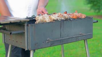 Man is Cooking Pork Barbecue in Summer in the Daytime Outdoors - Static Shot, Slow Motion. Turning Barbecue on Skewers. Hot Grilled Kebab on the Coals. Roasted or Grilled BBQ on a Skewer or Spit video