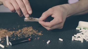 Man in Black Clothing is Rolling a Hand Made Cigarette Using Papers, Filters and Tobacco. A Way to Save on Tobacco Products. Tobacco Product Economy Concept. Close-Up Shot video