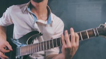 Medium Close-Up Shot of a Handsome Young Man Playing Electric Guitar in a Dark Smoky Room. Active Emotional Musician in a White Shirt is Recordind Music at the Home Studio Against the Black Background video