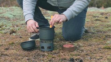uomo nel un' foresta è cucinando pasta con in scatola stufato utilizzando un' piccolo cucinare impostare. turista nel un' escursione è preparazione per il il pranzo. avvicinamento Visualizza, statico tiro video