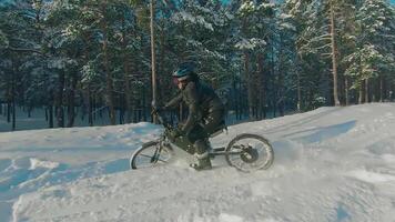 Cyclist in Black Clothes, Helmet and Snow Glasses Riding on Electric Bike in the Snow in Winter Forest. E-Bike Riding and Drifting at Cold Sunny Day - Super Slow Motion video