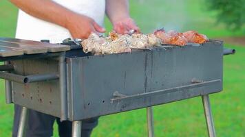 Man is Cooking Pork Barbecue in Summer in the Daytime Outdoors - Static Shot, Slow Motion. Turning Barbecue on Skewers. Hot Grilled Kebab on the Coals. Roasted or Grilled BBQ on a Skewer or Spit video