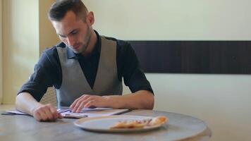 Handsome Young Man is Writing a Document in Pizzeria Cafe. Office Employee Has a Break. Middle Close-Up View, Dynamic Shot video