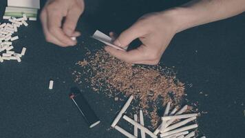 Man in Black Clothing is Rolling a Hand Made Cigarette Using Papers, Filters and Tobacco. A Way to Save on Tobacco Products. Tobacco Product Economy Concept. Top View video