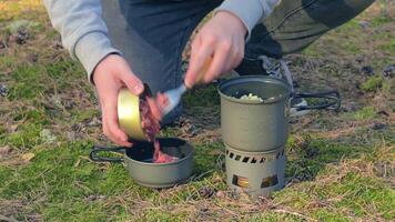 uomo nel un' foresta è cucinando pasta con in scatola stufato utilizzando un' piccolo cucinare impostare. turista nel un' escursione è preparazione per il il pranzo. avvicinamento Visualizza, statico tiro video