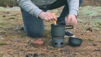 uomo nel un' foresta è cucinando pasta con in scatola stufato utilizzando un' piccolo cucinare impostare. turista nel un' escursione è preparazione per il il pranzo. avvicinamento Visualizza, statico tiro video