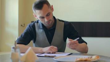 Handsome Young Man is Writing a Document in Pizzeria Cafe. Office Employee Has a Break. Middle Close-Up View, Dynamic Shot video
