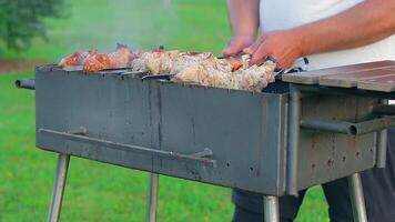 Man is Cooking Pork Barbecue in Summer in the Daytime Outdoors - Static Shot, Slow Motion. Turning Barbecue on Skewers. Hot Grilled Kebab on the Coals. Roasted or Grilled BBQ on a Skewer or Spit video