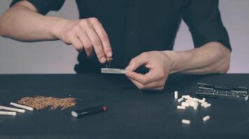 Man in Black Clothing is Rolling a Hand Made Cigarette Using Papers, Filters and Tobacco. A Way to Save on Tobacco Products. Tobacco Product Economy Concept - Slow Motion video