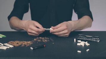 Man in Black Clothing is Rolling a Hand Made Cigarette Using Papers, Filters and Tobacco. A Way to Save on Tobacco Products. Tobacco Product Economy Concept - Slow Motion video