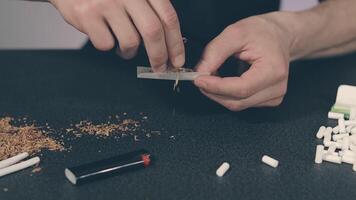 Man in Black Clothing is Rolling a Hand Made Cigarette Using Papers, Filters and Tobacco. A Way to Save on Tobacco Products. Tobacco Product Economy Concept - Slow Motion. Close-Up Shot video