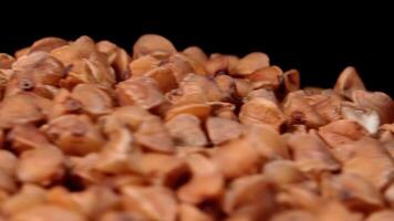 Dry Uncooked Brown Buckwheat Groats Heap on White Plate Rotating against Black Background - Macro. Raw Large Buckwheat Grains - Close-Up. Russian, Ukrainian and Belarusian Culture video