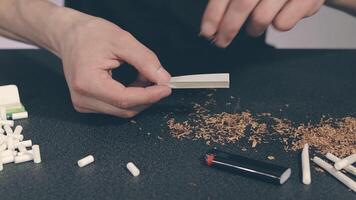 Man in Black Clothing is Rolling a Hand Made Cigarette Using Papers, Filters and Tobacco. A Way to Save on Tobacco Products. Tobacco Product Economy Concept. Close-Up Shot video