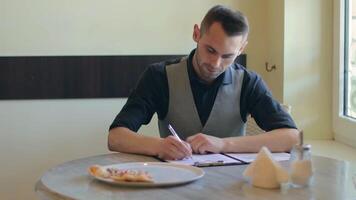 Handsome Young Man is Writing a Document in Pizzeria Cafe. Office Employee Has a Break. Middle Close-Up View, Dynamic Shot video