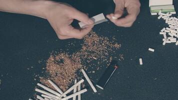 Man in Black Clothing is Rolling a Hand Made Cigarette Using Papers, Filters and Tobacco. A Way to Save on Tobacco Products. Tobacco Product Economy Concept. Top View video