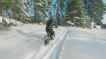Cyclist in Black Clothes, Helmet and Snow Glasses Riding on Electric Bike in the Snow in Winter Forest. E-Bike Riding and Drifting at Cold Sunny Day - Super Slow Motion video