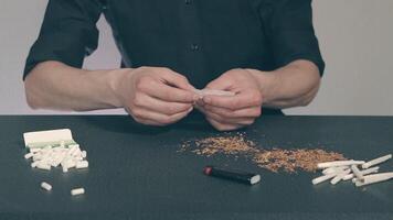 Man in Black Clothing is Rolling a Hand Made Cigarette Using Papers, Filters and Tobacco. A Way to Save on Tobacco Products. Tobacco Product Economy Concept video