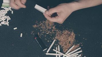 Man in Black Clothing is Rolling a Hand Made Cigarette Using Papers, Filters and Tobacco. A Way to Save on Tobacco Products. Tobacco Product Economy Concept. Top View video