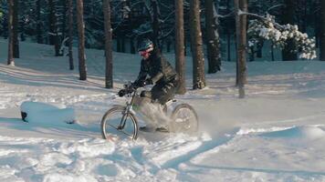 Cyclist in Black Clothes, Helmet and Snow Glasses Riding on Electric Bike in the Snow in Winter Forest. E-Bike Riding and Drifting at Cold Sunny Day - Slow Motion video