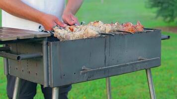Man is Cooking Pork Barbecue in Summer in the Daytime Outdoors - Static Shot, Slow Motion. Turning Barbecue on Skewers. Hot Grilled Kebab on the Coals. Roasted or Grilled BBQ on a Skewer or Spit video