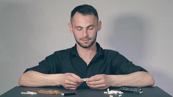 Man in Black Clothing is Rolling a Hand Made Cigarette Using Papers, Filters and Tobacco. A Way to Save on Tobacco Products. Tobacco Product Economy Concept. Middle Angle VIew, Static Shot video