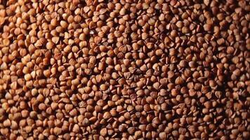 Dry Uncooked Brown Buckwheat Groats, Rotating Background - Top View, Low Key Light. Raw Large Buckwheat Grains. Russian, Ukrainian and Belarusian Culture. Rotation Left video