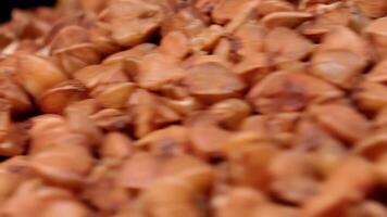 Dry Uncooked Brown Buckwheat Groats Heap on White Plate Rotating against Black Background - Macro. Raw Large Buckwheat Grains - Close-Up. Russian, Ukrainian and Belarusian Culture video