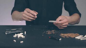 Man in Black Clothing is Rolling a Hand Made Cigarette Using Papers, Filters and Tobacco. A Way to Save on Tobacco Products. Tobacco Product Economy Concept - Slow Motion video