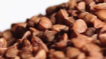 Dry Uncooked Brown Buckwheat Groats Heap on White Plate Rotating against Black Background - Macro. Raw Large Buckwheat Grains - Close-Up. Russian, Ukrainian and Belarusian Culture video