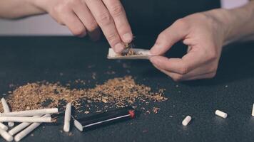 Man in Black Clothing is Rolling a Hand Made Cigarette Using Papers, Filters and Tobacco. A Way to Save on Tobacco Products. Tobacco Product Economy Concept. Close-Up Shot video