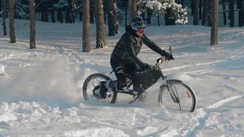 Cyclist in Black Clothes, Helmet and Snow Glasses Riding on Electric Bike in the Snow in Winter Forest. E-Bike Riding and Drifting at Cold Sunny Day - Slow Motion video