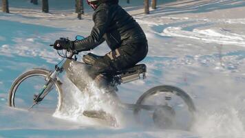 Cyclist in Black Clothes, Helmet and Snow Glasses Riding on Electric Bike in the Snow in Winter Forest. E-Bike Riding and Drifting at Cold Sunny Day - Slow Motion video