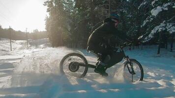 Cyclist in Black Clothes, Helmet and Snow Glasses Riding on Electric Bike in the Snow in Winter Forest. E-Bike Riding and Drifting at Cold Sunny Day - Super Slow Motion video