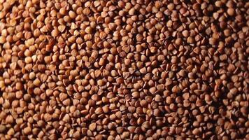 Dry Uncooked Brown Buckwheat Groats, Rotating Background - Top View, Low Key Light. Raw Large Buckwheat Grains. Russian, Ukrainian and Belarusian Culture. Rotation Right video