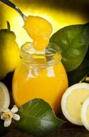 A jar of lemon curd with a spoon and some lemons photo