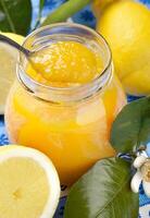 A jar of lemon curd with a spoon and lemons photo