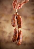 A hand holding three sausages on a string photo