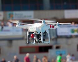 A white and red drone flying over a crowd photo