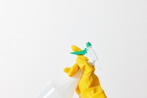 Woman holding a spray bottle with a green and yellow sprayer on white background. yellow gloves photo