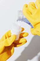 Woman in yellow rubber gloves holds a bottle of cleaning solution with a yellow cap, standing in photo