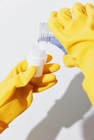 Woman in yellow gloves pouring cleaning solution from bottle into container on white surface. house photo