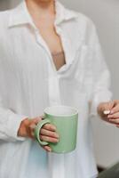Woman in white shirt holding green coffee mug in front of computer screen with keyboard and mouse in photo