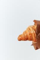 Hand holding croissant in brown paper bag on white background with text space. photo