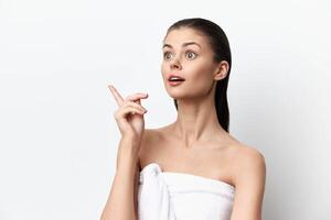 surprised young woman pointing upwards with an expression of excitement, wrapped in a towel against photo