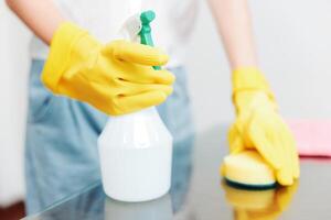 Woman cleaning bottle with sponge and rag on table wearing yellow rubber gloves. photo