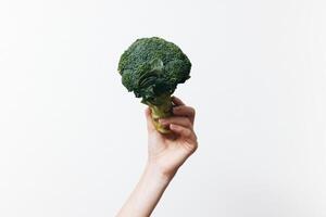 Broccoli piece held by person against white background. hand in focus. photo