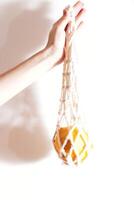 Hand holding white net bag with oranges, isolated on white background. photo